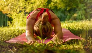 Woman doing a forward fold stretch outside on a yoga mat.